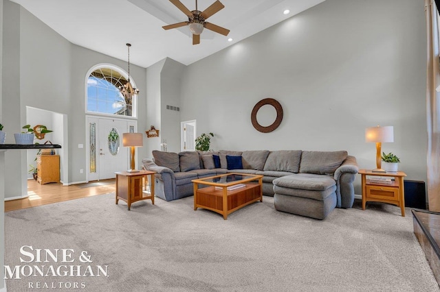 carpeted living area featuring baseboards, recessed lighting, ceiling fan with notable chandelier, a towering ceiling, and wood finished floors