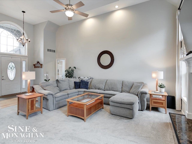 living area featuring visible vents, carpet floors, recessed lighting, ceiling fan with notable chandelier, and a towering ceiling