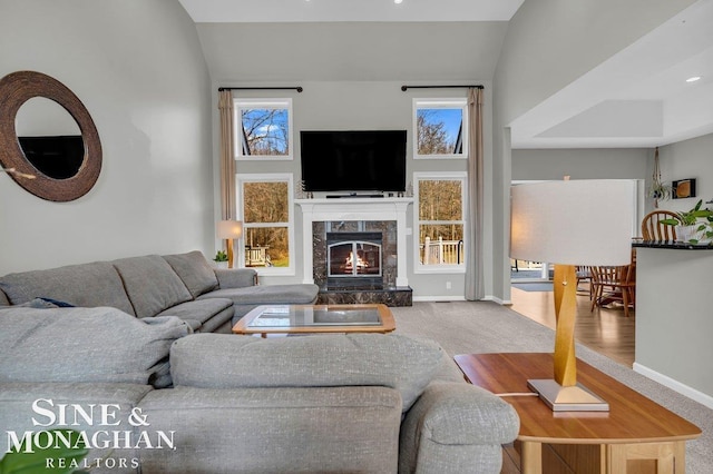 living room featuring a high end fireplace, vaulted ceiling, baseboards, and carpet floors