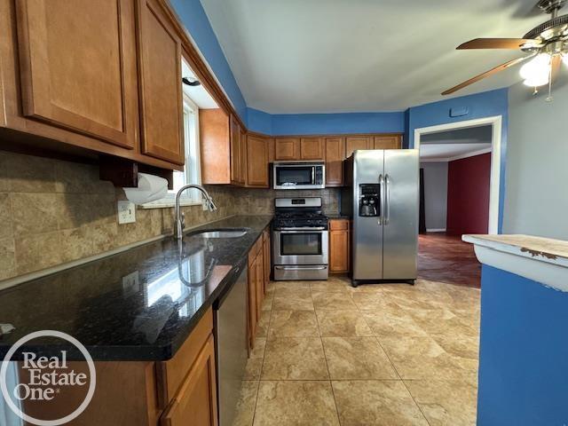 kitchen with backsplash, dark stone counters, brown cabinets, stainless steel appliances, and a sink