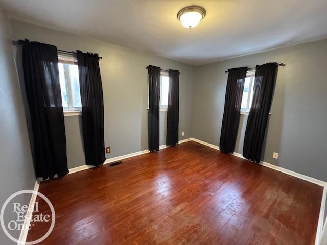 unfurnished room featuring wood finished floors, visible vents, and baseboards