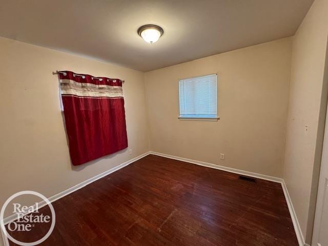 empty room featuring visible vents, wood finished floors, and baseboards