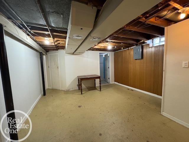 below grade area featuring electric panel, wooden walls, and baseboards