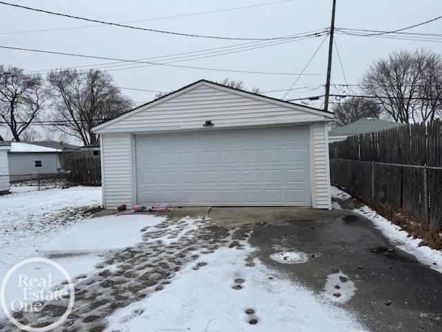 snow covered garage featuring a detached garage and fence