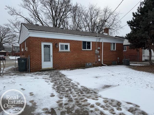 snow covered property featuring central air condition unit, fence, brick siding, and a chimney