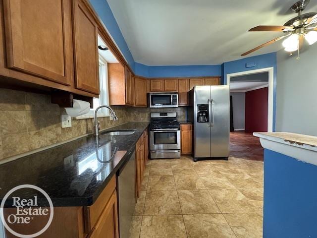 kitchen featuring a sink, dark stone countertops, backsplash, appliances with stainless steel finishes, and brown cabinetry