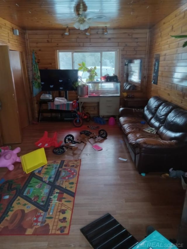 living room with wood finished floors, wooden walls, wood ceiling, and ceiling fan