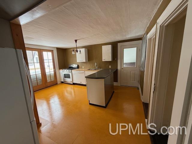 kitchen featuring white appliances, a peninsula, a sink, pendant lighting, and dark countertops