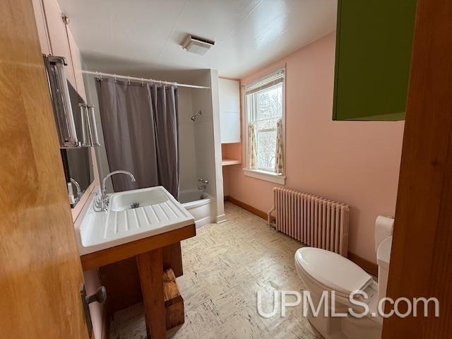 bathroom featuring shower / bath combo with shower curtain, toilet, a sink, radiator heating unit, and baseboards