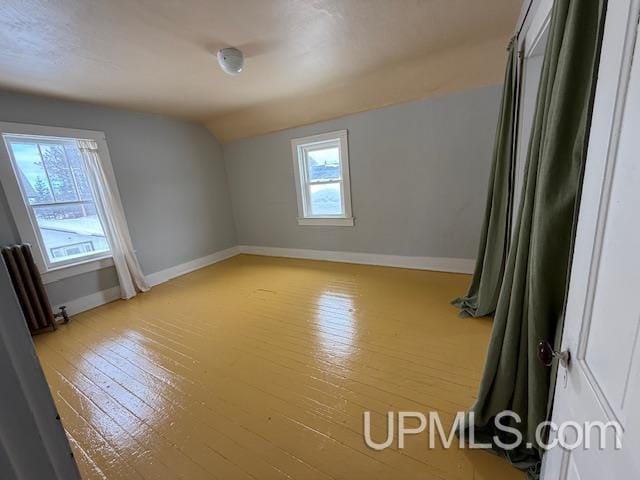 spare room with baseboards, wood-type flooring, radiator heating unit, and vaulted ceiling