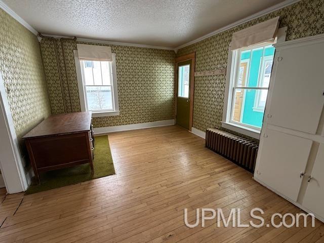 empty room with wallpapered walls, radiator heating unit, a textured ceiling, crown molding, and light wood-type flooring