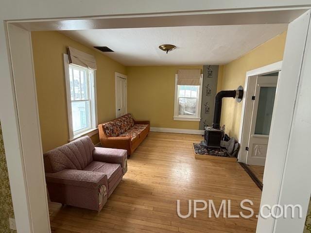 living room featuring baseboards, plenty of natural light, light wood-style flooring, and a wood stove