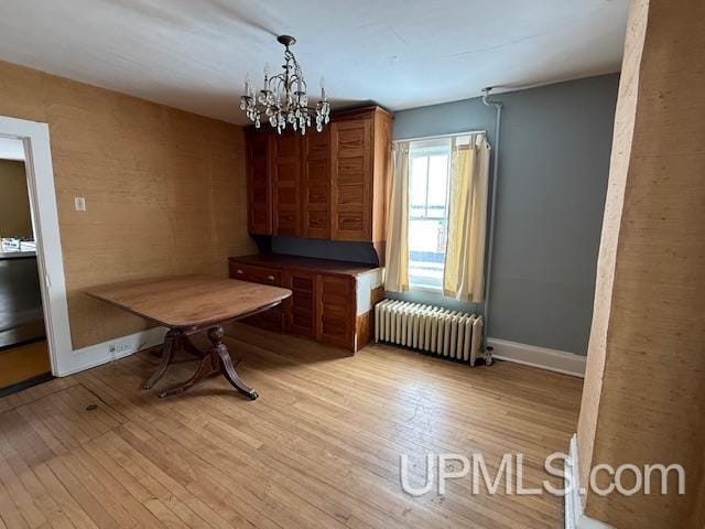 unfurnished dining area featuring baseboards, light wood-type flooring, radiator heating unit, and an inviting chandelier