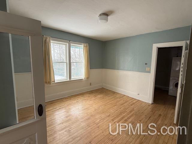 unfurnished room with stacked washer / drying machine, wood finished floors, and wainscoting