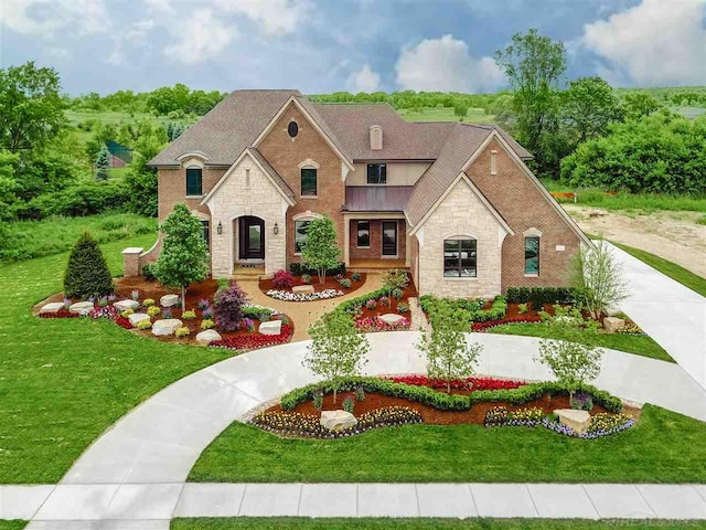 french country inspired facade featuring a front lawn, a standing seam roof, stone siding, a shingled roof, and brick siding