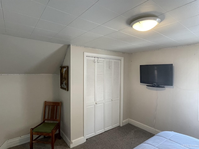 bedroom with a closet, dark carpet, lofted ceiling, and baseboards