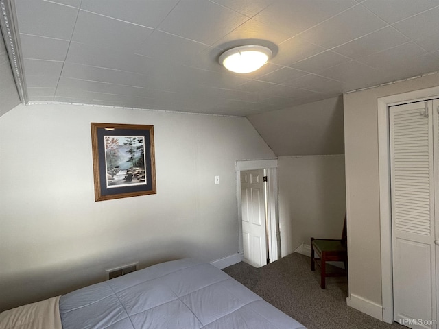 bedroom featuring visible vents, lofted ceiling, a closet, carpet, and baseboards