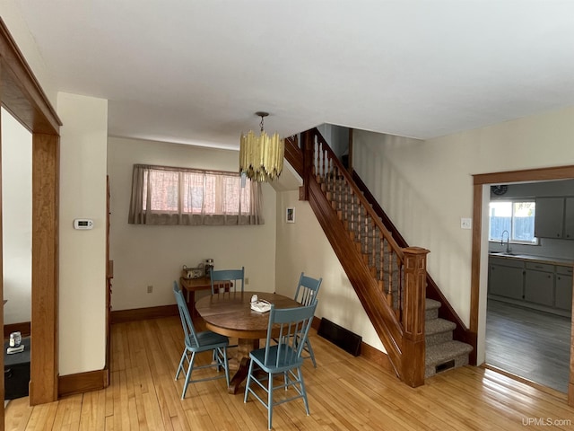 dining space featuring stairway, baseboards, light wood finished floors, and a chandelier