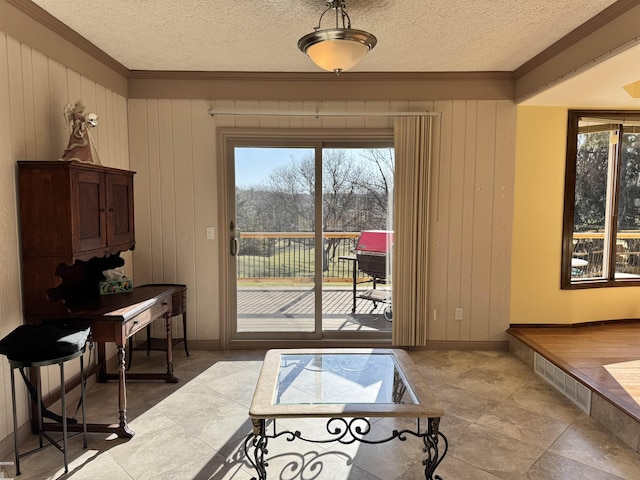 doorway to outside featuring a textured ceiling, a healthy amount of sunlight, and ornamental molding