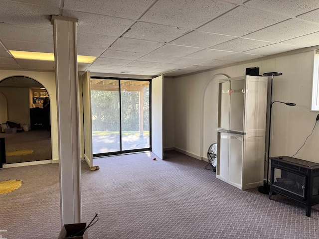 unfurnished living room featuring floor to ceiling windows, carpet floors, a wood stove, arched walkways, and a paneled ceiling