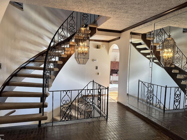 staircase with baseboards, arched walkways, a chandelier, and crown molding