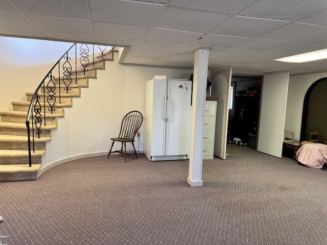 finished basement with freestanding refrigerator, baseboards, carpet floors, a paneled ceiling, and stairs