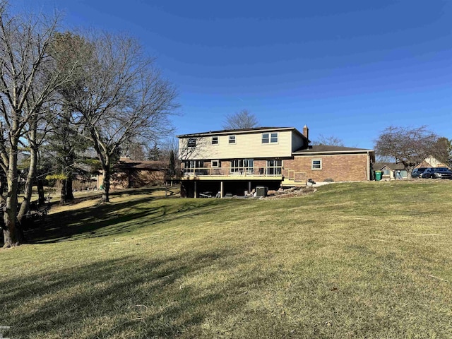 back of property featuring a yard, brick siding, a chimney, and a wooden deck