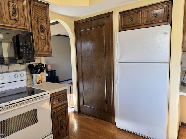 kitchen featuring white appliances, wood finished floors, arched walkways, light countertops, and backsplash