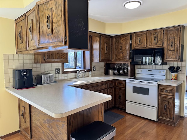 kitchen with electric stove, a sink, a peninsula, black microwave, and light countertops