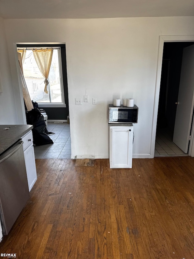 kitchen featuring dark wood-type flooring, stainless steel dishwasher, dark countertops, white cabinets, and baseboards