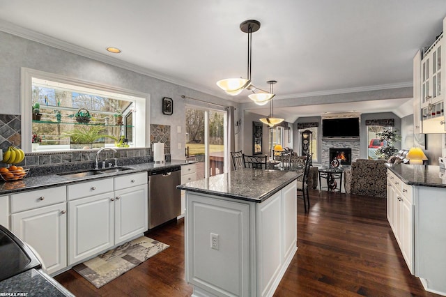 kitchen with a lit fireplace, a sink, white cabinets, dishwasher, and a center island