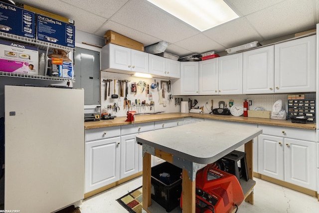 kitchen with decorative backsplash, light countertops, a paneled ceiling, concrete flooring, and white cabinetry