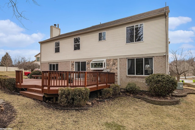 rear view of property with brick siding, a lawn, a chimney, and a deck