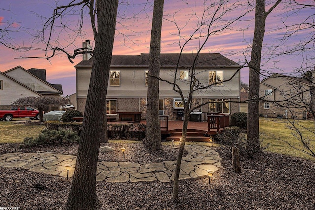 back of property at dusk with brick siding, a chimney, and a wooden deck