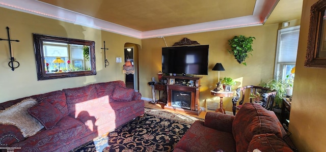 living area featuring arched walkways, a fireplace, baseboards, and a tray ceiling