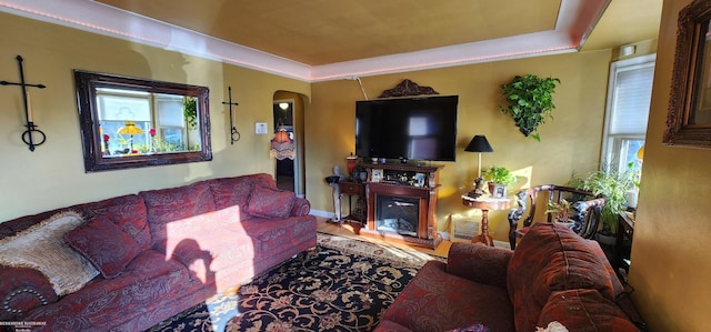 living room featuring a glass covered fireplace, a raised ceiling, baseboards, and arched walkways