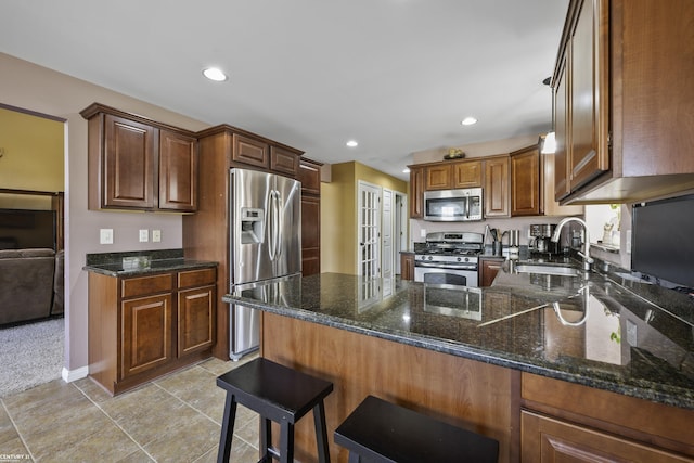 kitchen featuring dark stone counters, recessed lighting, a peninsula, stainless steel appliances, and a sink