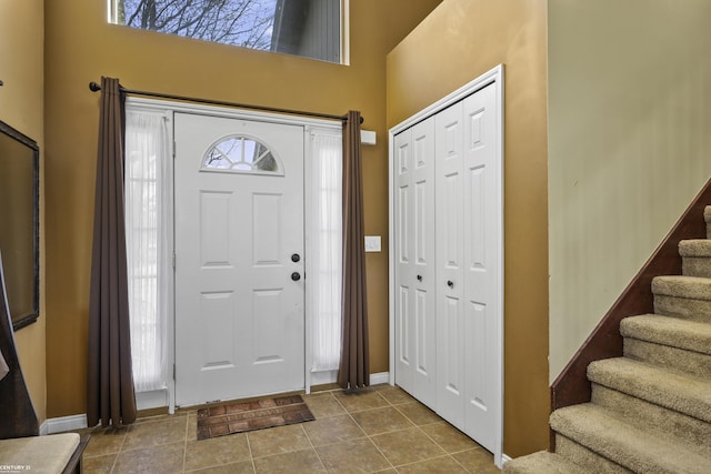 foyer entrance with stairs, dark tile patterned floors, baseboards, and a towering ceiling