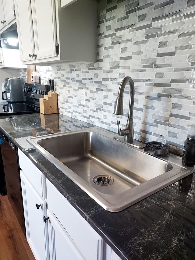 kitchen with under cabinet range hood, backsplash, white cabinetry, and a sink