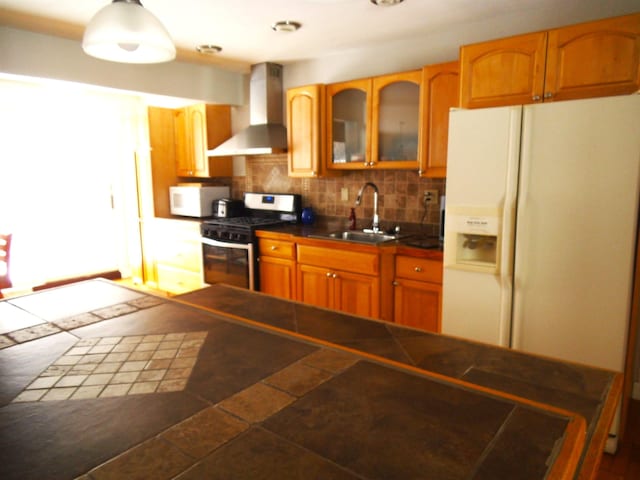 kitchen with white appliances, a sink, decorative backsplash, glass insert cabinets, and wall chimney range hood