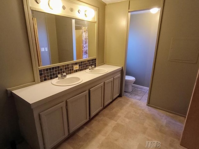 bathroom with double vanity, backsplash, toilet, and a sink