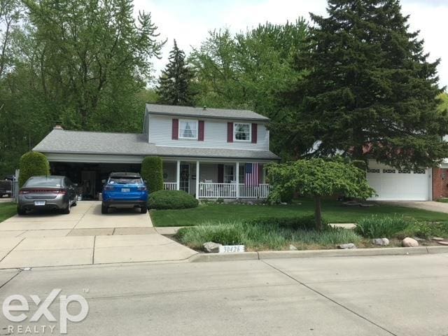 traditional-style house featuring a front lawn, an attached garage, covered porch, and driveway