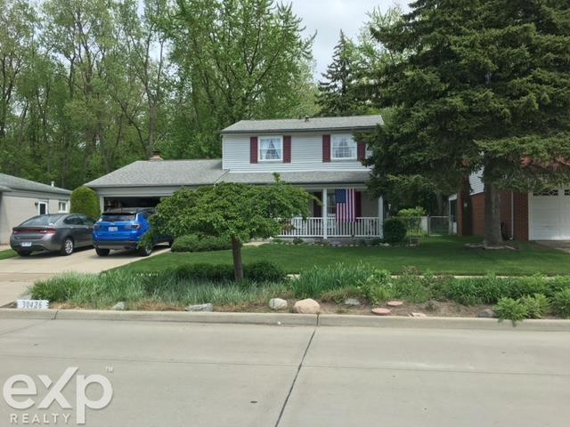 view of front of property featuring driveway, an attached garage, covered porch, and a front lawn