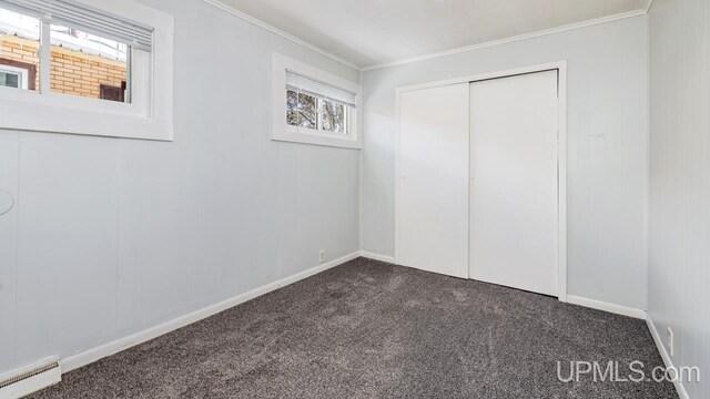 unfurnished bedroom featuring ornamental molding, dark carpet, a closet, baseboards, and baseboard heating