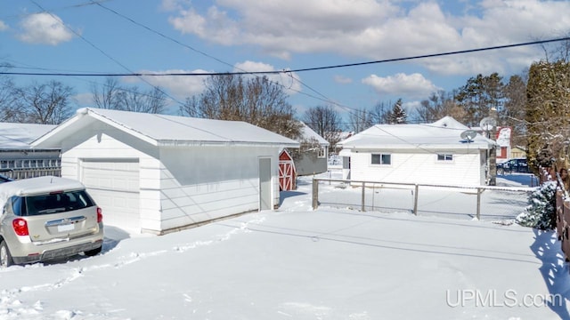 view of snowy exterior featuring a garage, an outbuilding, and fence