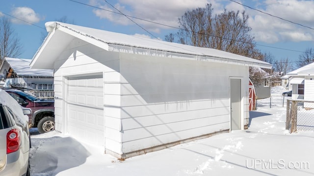 snow covered garage with a detached garage and fence