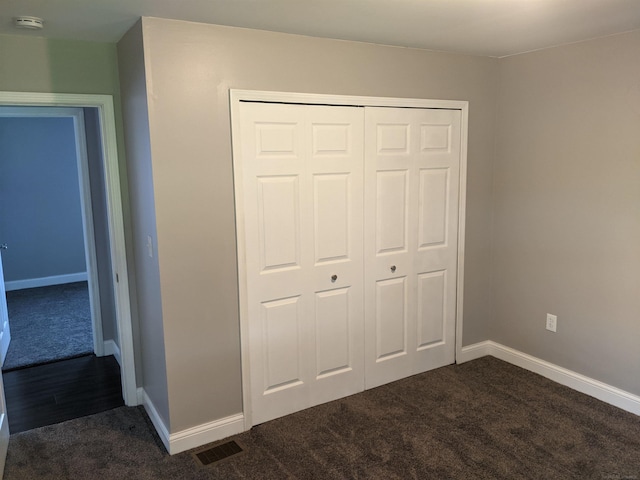 unfurnished bedroom featuring visible vents, dark colored carpet, a closet, and baseboards