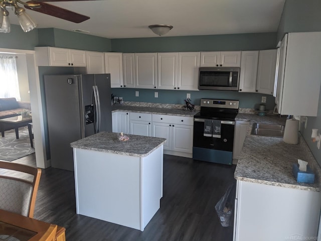 kitchen with a ceiling fan, a kitchen island, dark wood-style floors, stainless steel appliances, and white cabinets