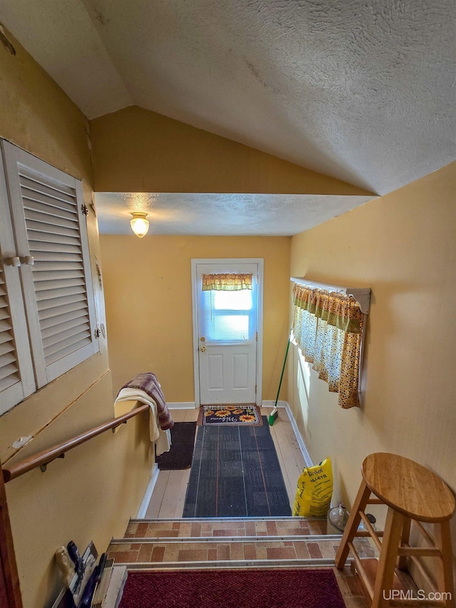 entryway with baseboards, a textured ceiling, wood finished floors, and vaulted ceiling