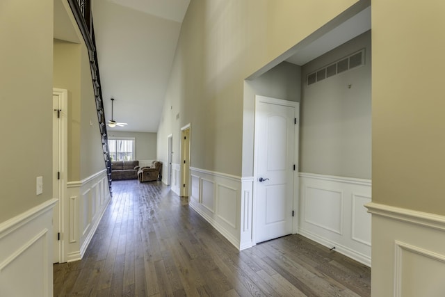 corridor with a decorative wall, visible vents, dark wood-type flooring, and a wainscoted wall